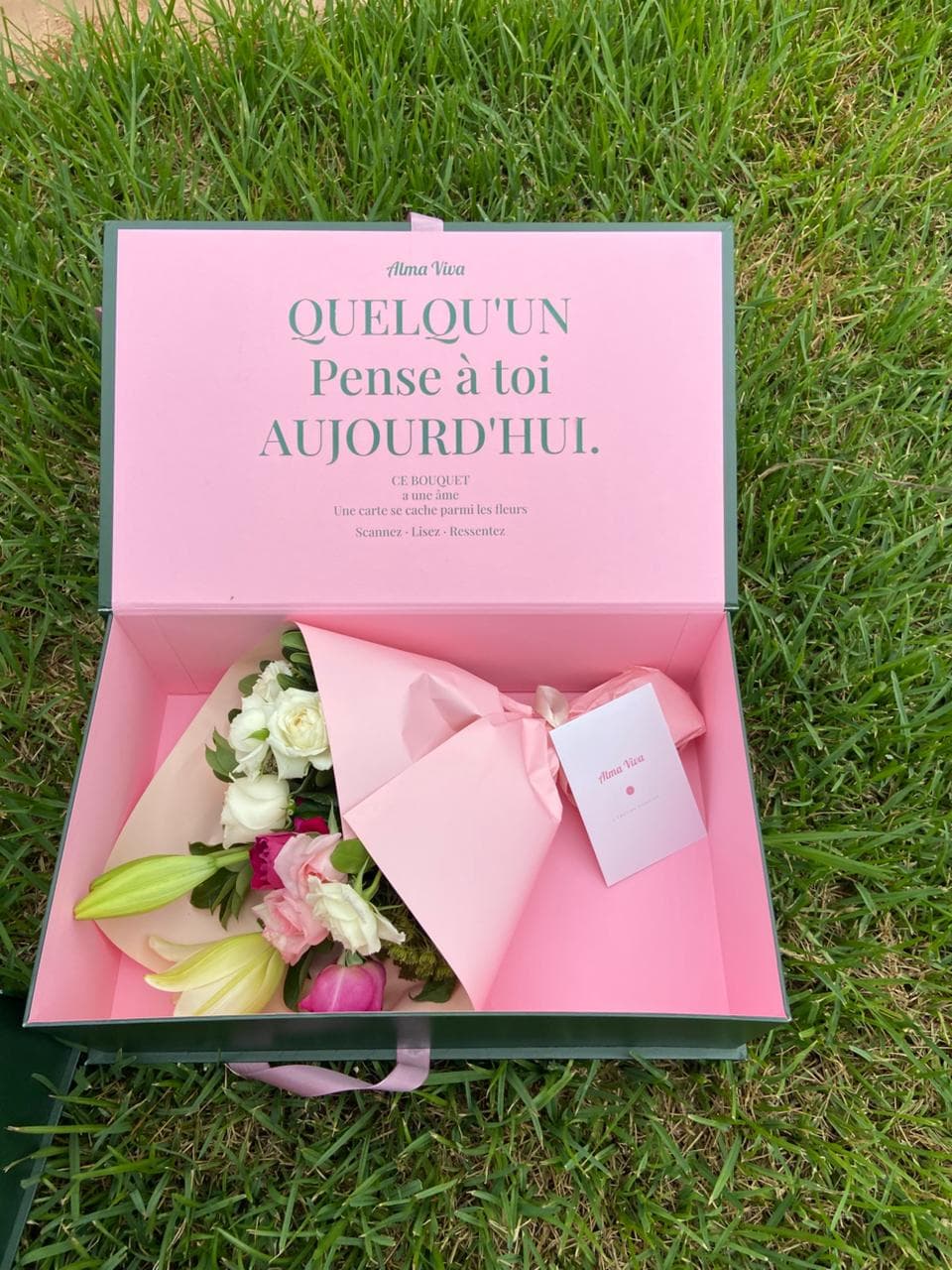 Boîte signature Alma Viva ouverte sur l'herbe, bouquet et carte à l'intérieur